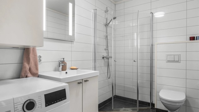 Badet i underetasjen er fra byggeår og har servantinnredning, dusjhjørne, vegghengt toalett og opplegg for vaskemaskin.