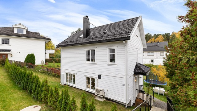 Overbygd inngangsparti med utvendig trapp og hekk mot nabogrensen. Egen parkeringsplass med elbillader rett i overkant.