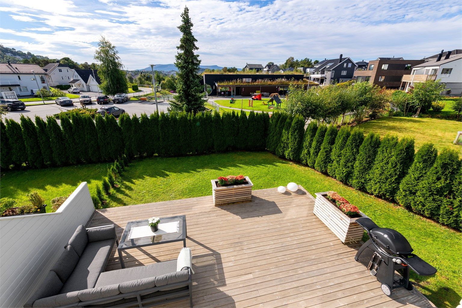 Utsikt fra veranda i 1. etasje til markterrasse og hage som er opparbeidet med plen og inngjerdet med hekk. Flott skjermet og barnevennlig uteområde