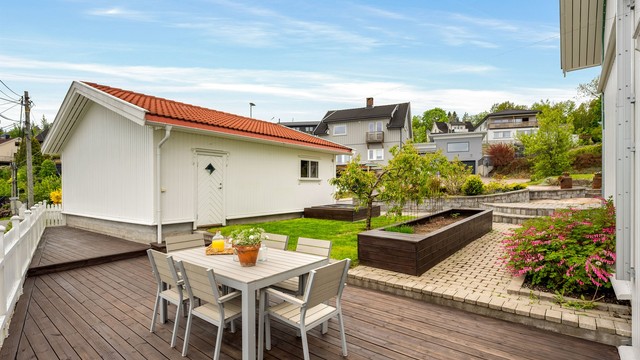 Tomten er pent opparbeidet med plenarealer, beplantning og steinlagte soner.