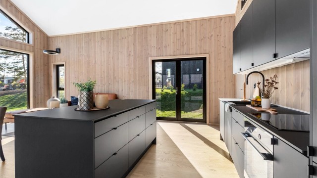 Kjøkkenet er praktisk og står fint til de panelte veggene, samtidig som det tøffer opp stilen litt med de matte og slette flatene. Kjøkkenøya lager et fint skille i rommet.