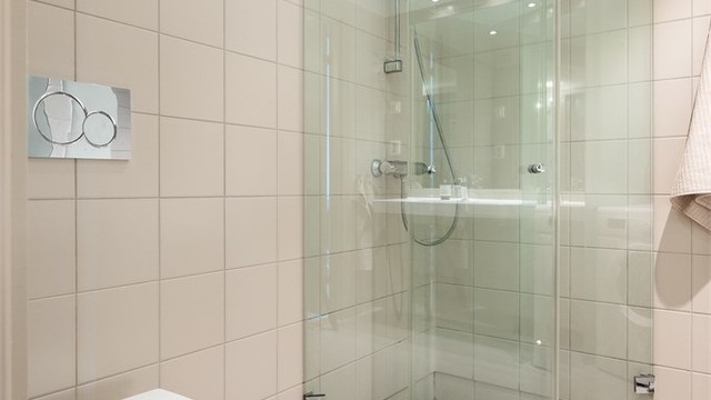 Badet har elektrisk gulvvarme for økt komfort. Innredningen inkluderer vegghengt klosett og dusjhjørne med svingbare glassdører.
