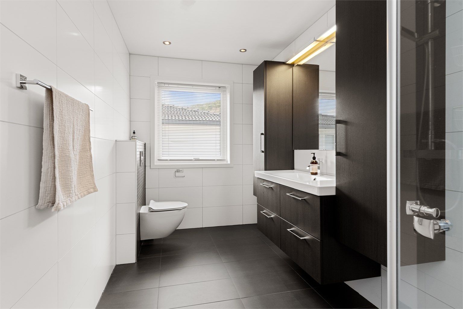 Flislagt bad med varme i gulvet, vegghengt toalett og downlights i taket.