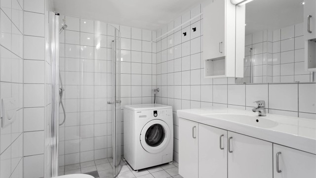 Badet har vegghengt toalett, dusjhjørne og vaskemaskin.