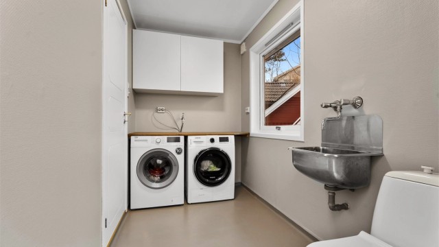 Fra kjøkkenet er det inngang til et praktisk vaskerom med plass til vaskemaskin og tørketrommel. Det er utslagsvask, praktisk arbeidsbenk, toalett og overskap. Egen utgang til siden av huset.