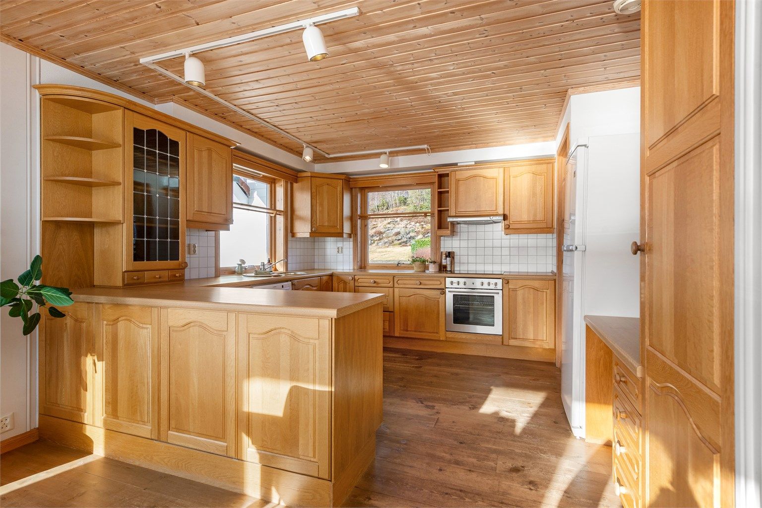 Kjøkkeninnredning med profilerte eikefronter og benkeplate av laminat. Kjøkkenhalvøy mot spisestue