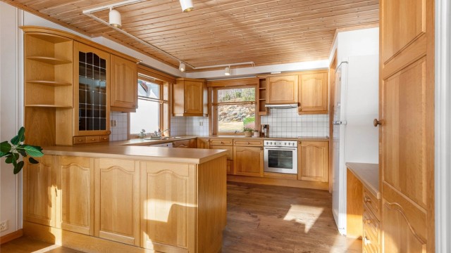 Kjøkkeninnredning med profilerte eikefronter og benkeplate av laminat. Kjøkkenhalvøy mot spisestue