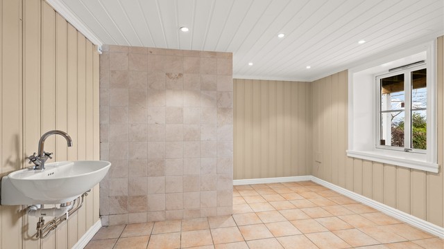Badet i kjelleren har flislagt gulv med varmekabler og veggmontert servant.