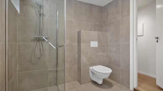 Badet er innredet med vegghengt toalett, plassbygget servantinnredning og dusjhjørne med glassvegg.