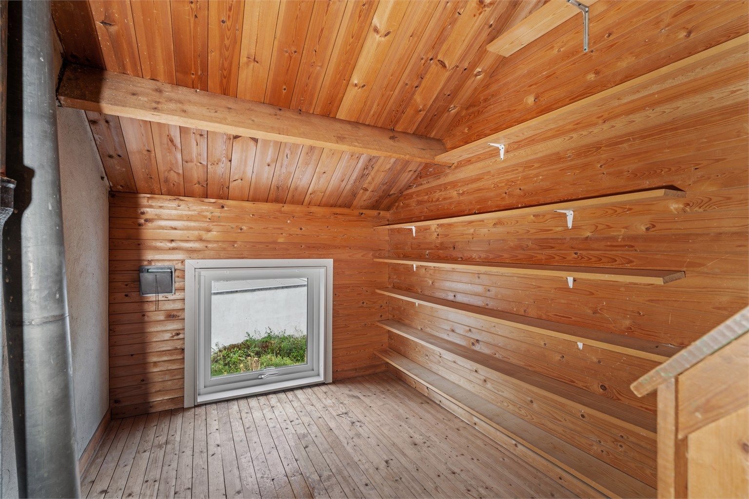 Loftsetasjen har panelte vegger, faste vegghyller og vindu.