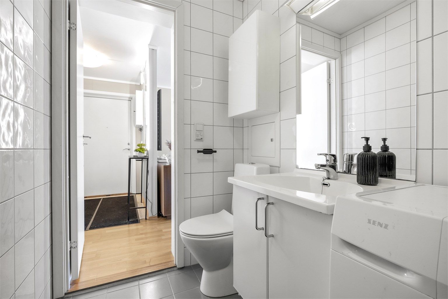 Badet er innredet med vegghengt servant, speil med overlys og gulvstående toalett.