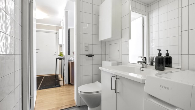 Badet er innredet med vegghengt servant, speil med overlys og gulvstående toalett.