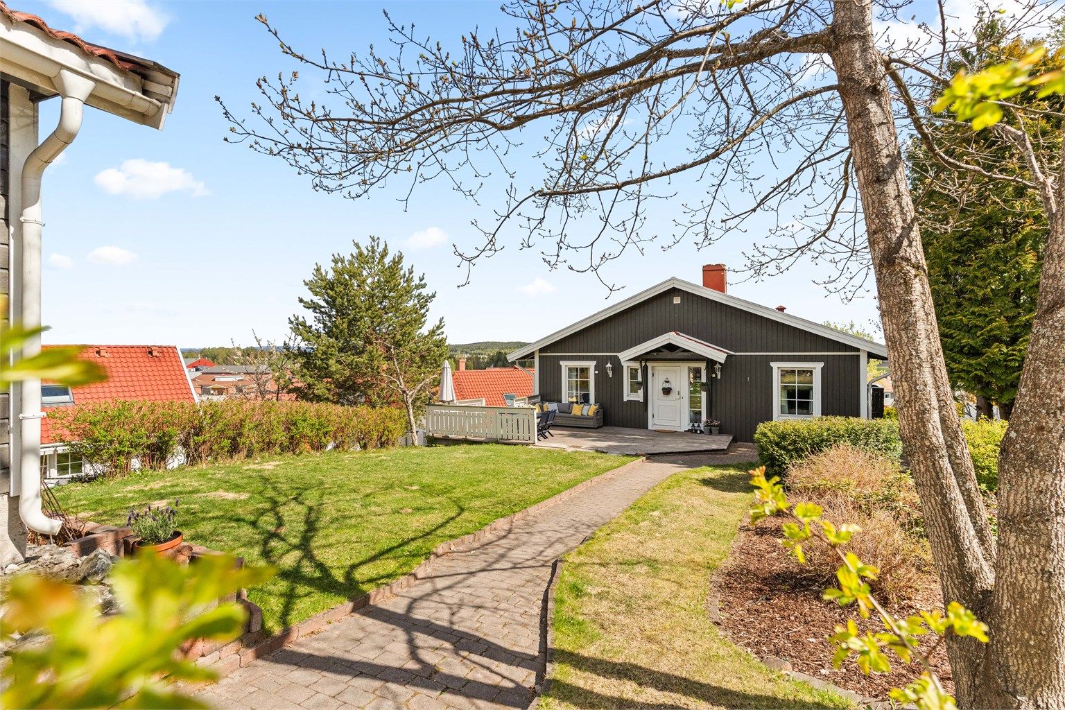 Tomten er opparbeidet med plenarealer, beplantning og gangsti av belegningsstein.