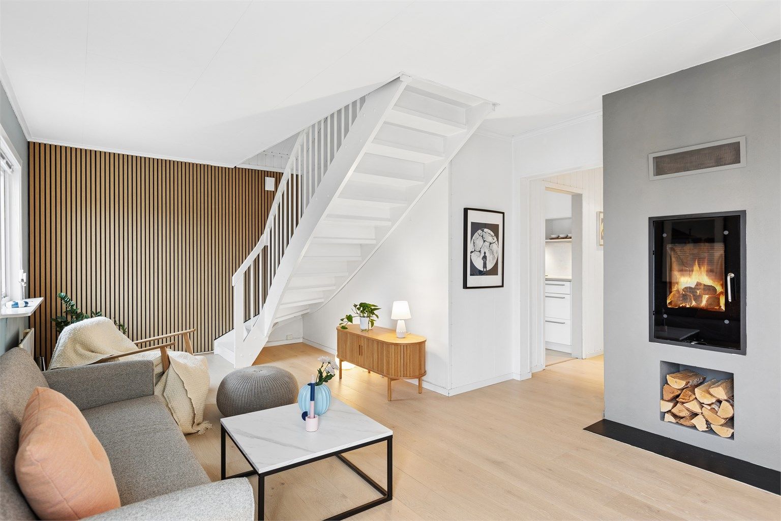 Stuen har hvitmalt trapp til loftsetasjen, spilevegg og etablert ildsted.