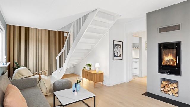 Stuen har hvitmalt trapp til loftsetasjen, spilevegg og etablert ildsted.