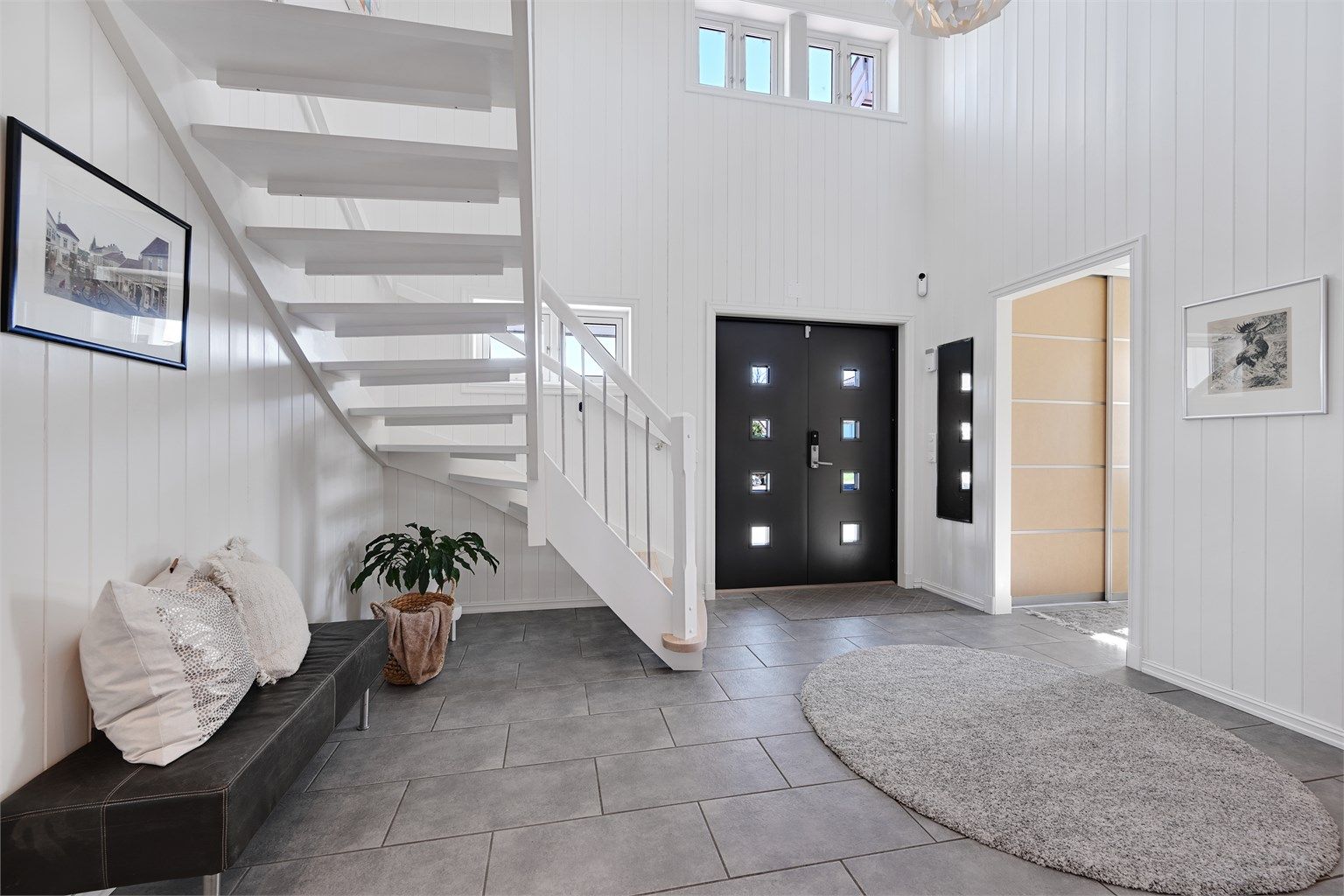 En lys og åpen hall med dobbel takhøyde og ny, malt hovedytterdør fra 2022 ønsker velkommen.