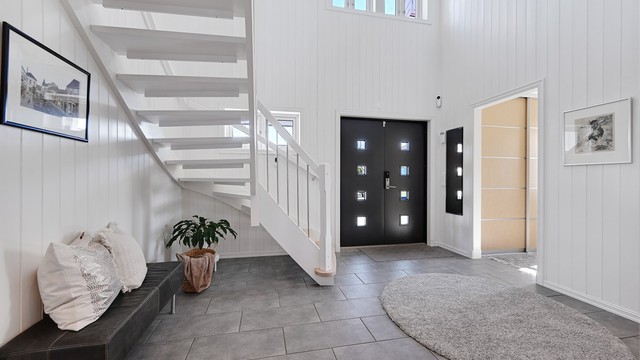 En lys og åpen hall med dobbel takhøyde og ny, malt hovedytterdør fra 2022 ønsker velkommen.