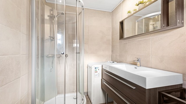 Badet har en funksjonell utforming med dusjkabinett, toalett, vaskemaskin og servantinnredning med oppbevaringsplass.