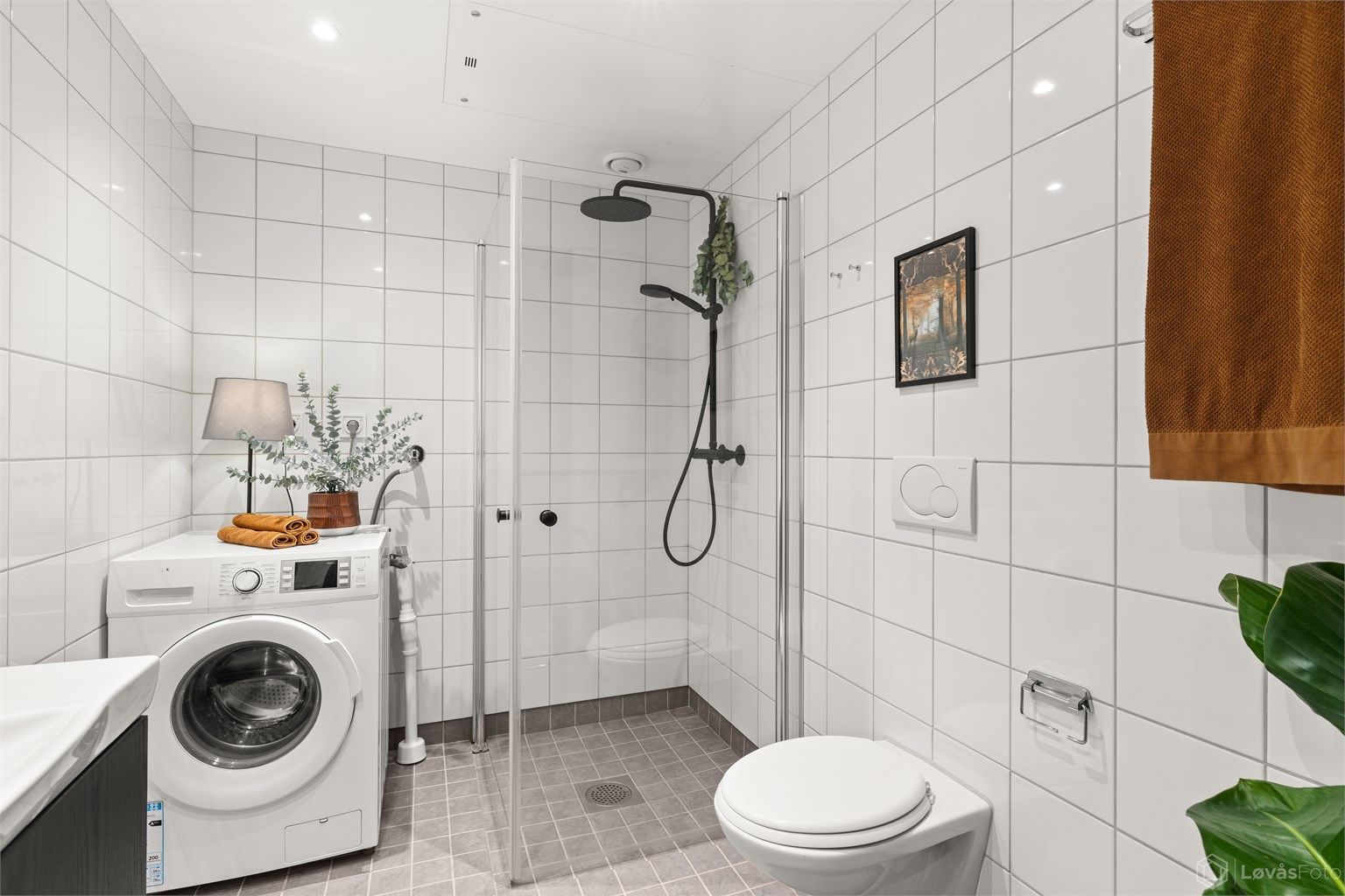 Badet er utstyrt med vegghengt servantinnredning med speil, dusjhjørne med glassdører og vegghengt dusjarmatur med hånddusj og regndusj, samt vegghengt toalett. Vaskemaskin medfølger. 