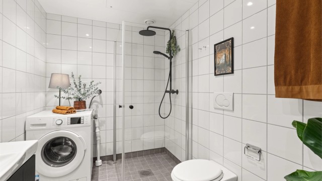 Badet er utstyrt med vegghengt servantinnredning med speil, dusjhjørne med glassdører og vegghengt dusjarmatur med hånddusj og regndusj, samt vegghengt toalett. Vaskemaskin medfølger.