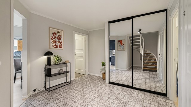 Romslig gang med stor skyvedørsgarderobe med speilfronter og mønstret gulvbelegg.
