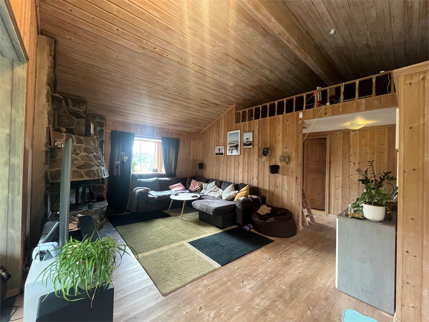 Romslig stue med plass til sofa og tilhørende møblement. Pen peis i hjørnet. 