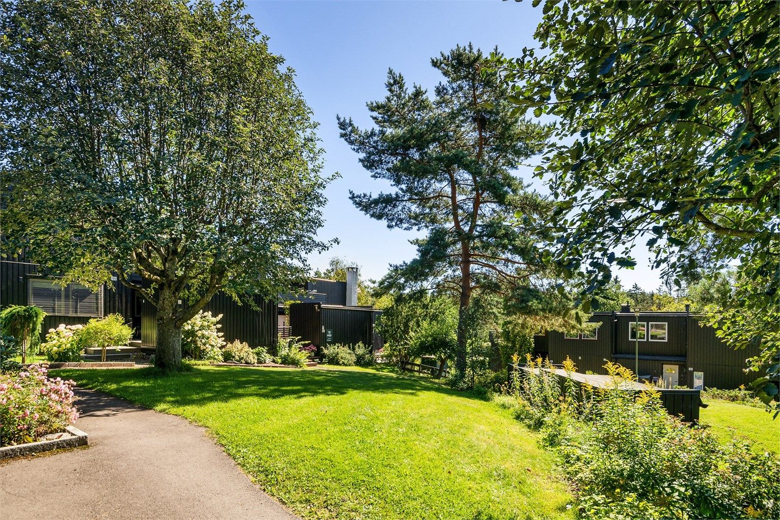 Det er et flott grøntområde foran boligen med fine prydbusker og trær.