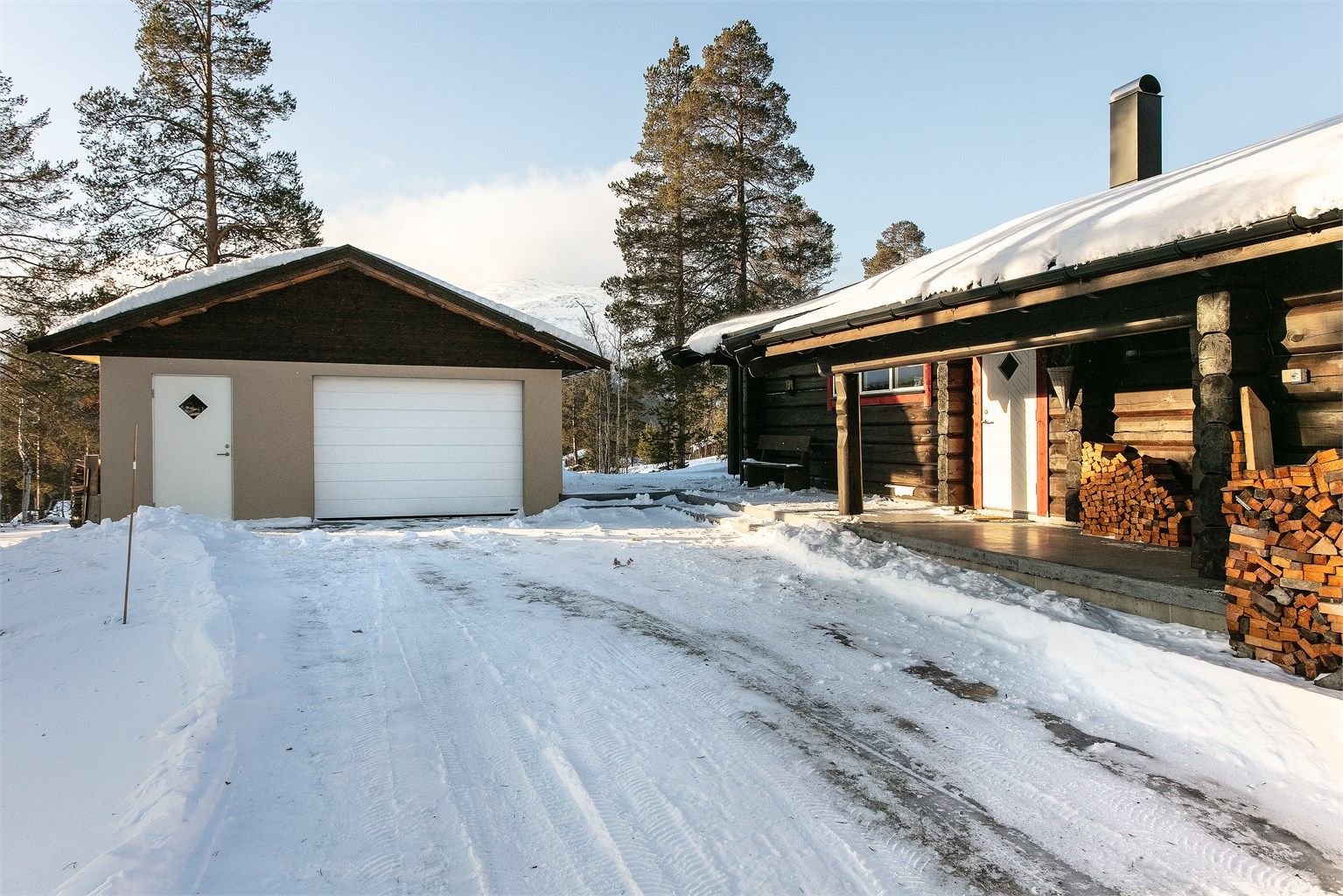 Gårdsplass med garasje og fasade/inngangsparti til hytten