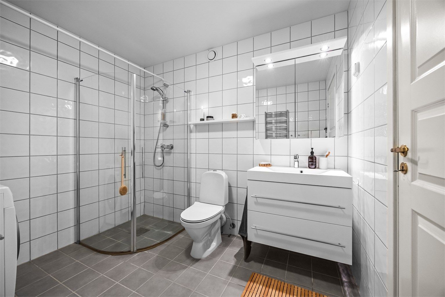 Badet har hvit glatt innredning med skuffer, speilskap og innfellbare dusjvegger.