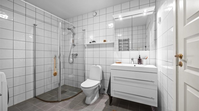 Badet har hvit glatt innredning med skuffer, speilskap og innfellbare dusjvegger.