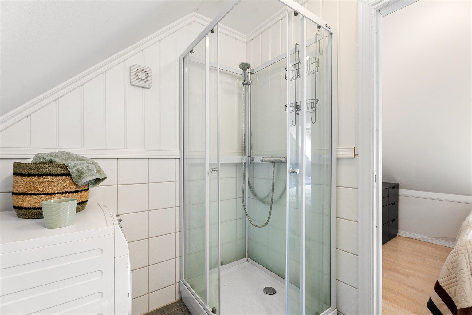 Dusjsone med plassbesparende, innfellbare glassdører og ren flisutførelse.