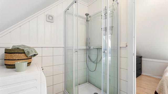 Dusjsone med plassbesparende, innfellbare glassdører og ren flisutførelse.