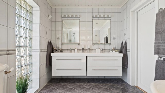 Videre er det et toalett i retrodesign, to servanter på hver sin hvite skuffeseksjon og to fastflisede speil med overlys.