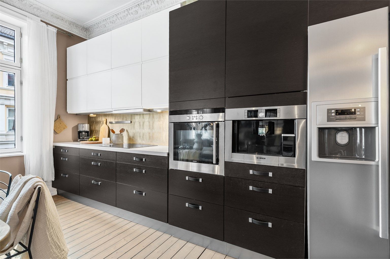 Åpen kjøkkenløsning. Innredningen er fra ukjent årstall med slette fronter. Benkeplate av stein. Nedfelt oppvaskkum med ett-greps kjøkkenarmatur.