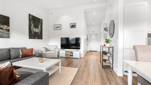 Den romslige stuen har god takhøyde, malte overflater og integrerte downlights som bidrar til en lys og innbydende atmosfære.
