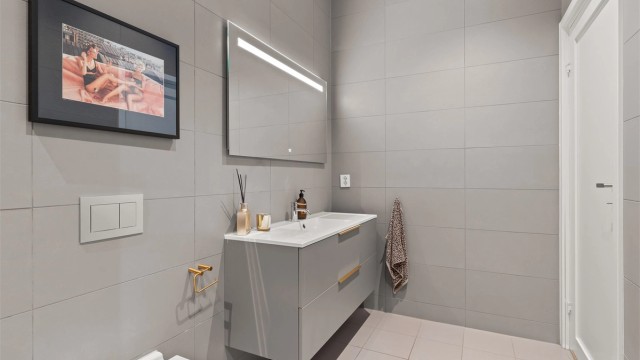 Lekkert og stilrent bad med flislagte gulv og vegger, elektrisk gulvvarme og himling med integrerte downlights.