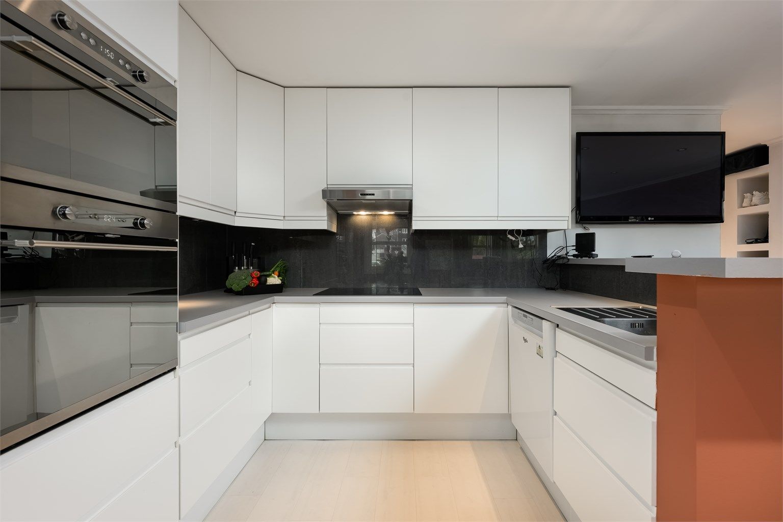 Moderne kjøkken med glatte, hvite fronter og integrerte hvitevarer. 