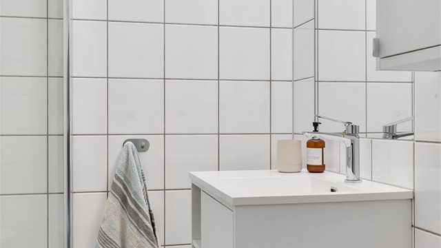 Badet har vegghengt servant med armatur og speil med overlys.