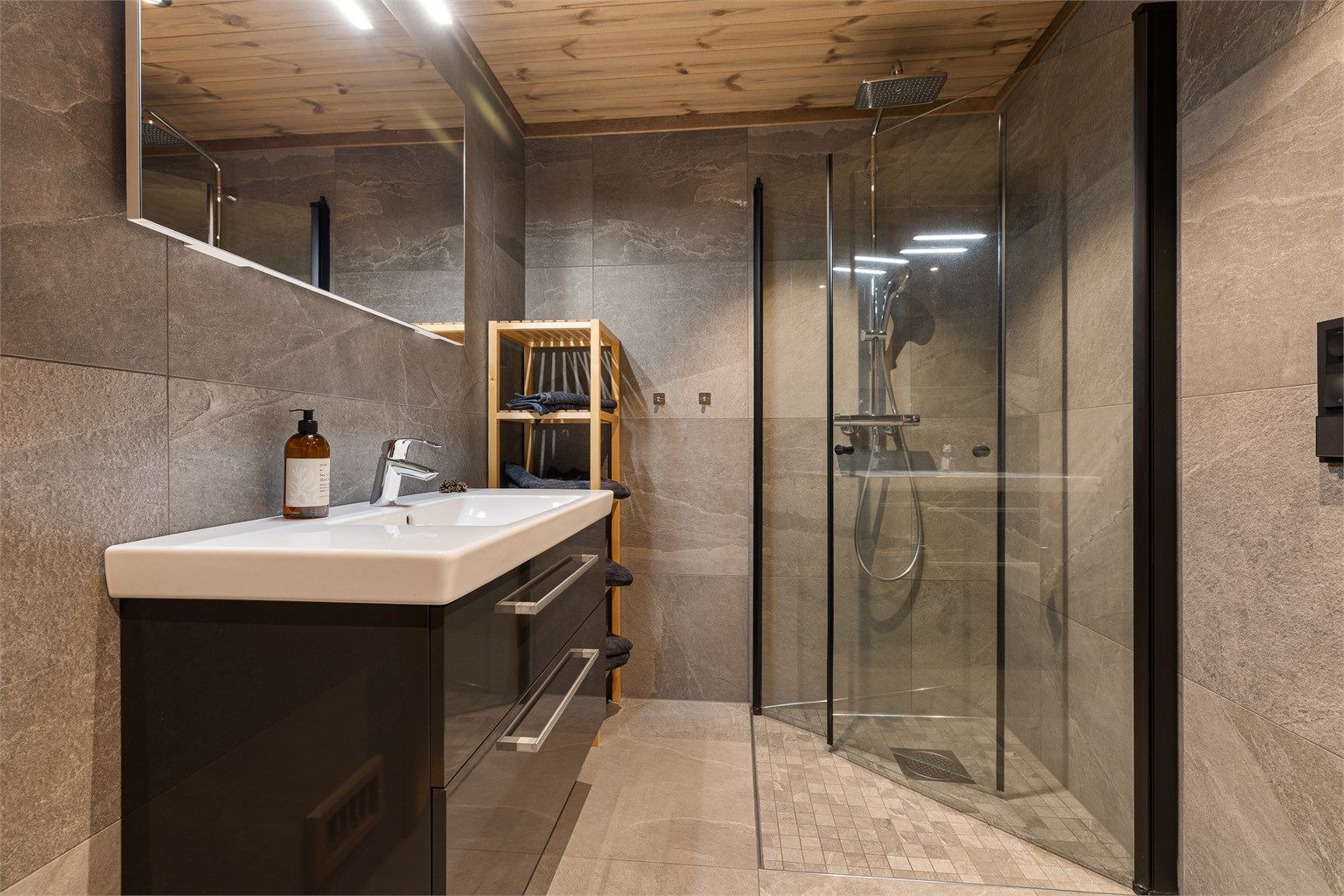 Badet har toalett, downlights og gulvvarme, servant med skuffer og et speil med integrert belysning. Dusjhjørne med innfelte glassdører.