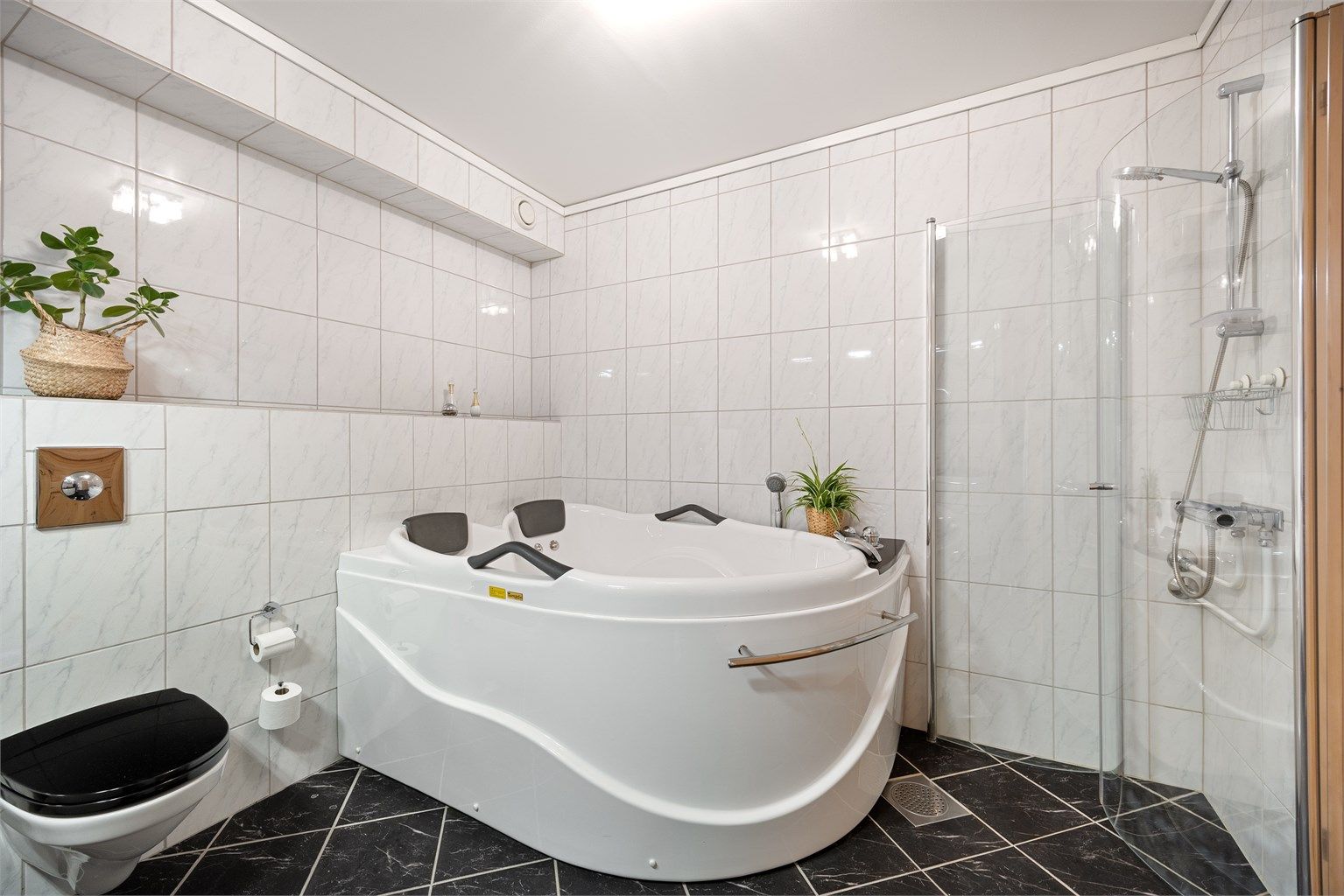 Badet er utstyrt med vegghengt toalett og servantinnredning, badekar med innebygget badekararmatur og dusjhjørne.