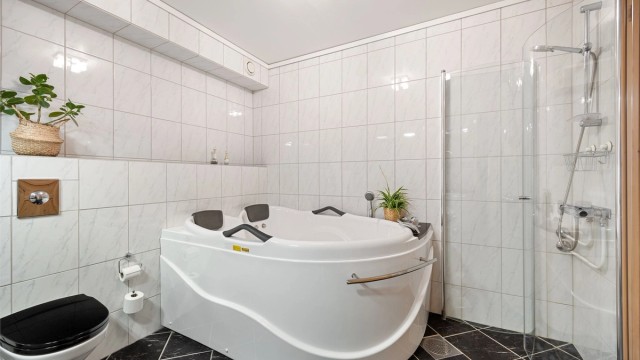 Badet er utstyrt med vegghengt toalett og servantinnredning, badekar med innebygget badekararmatur og dusjhjørne.