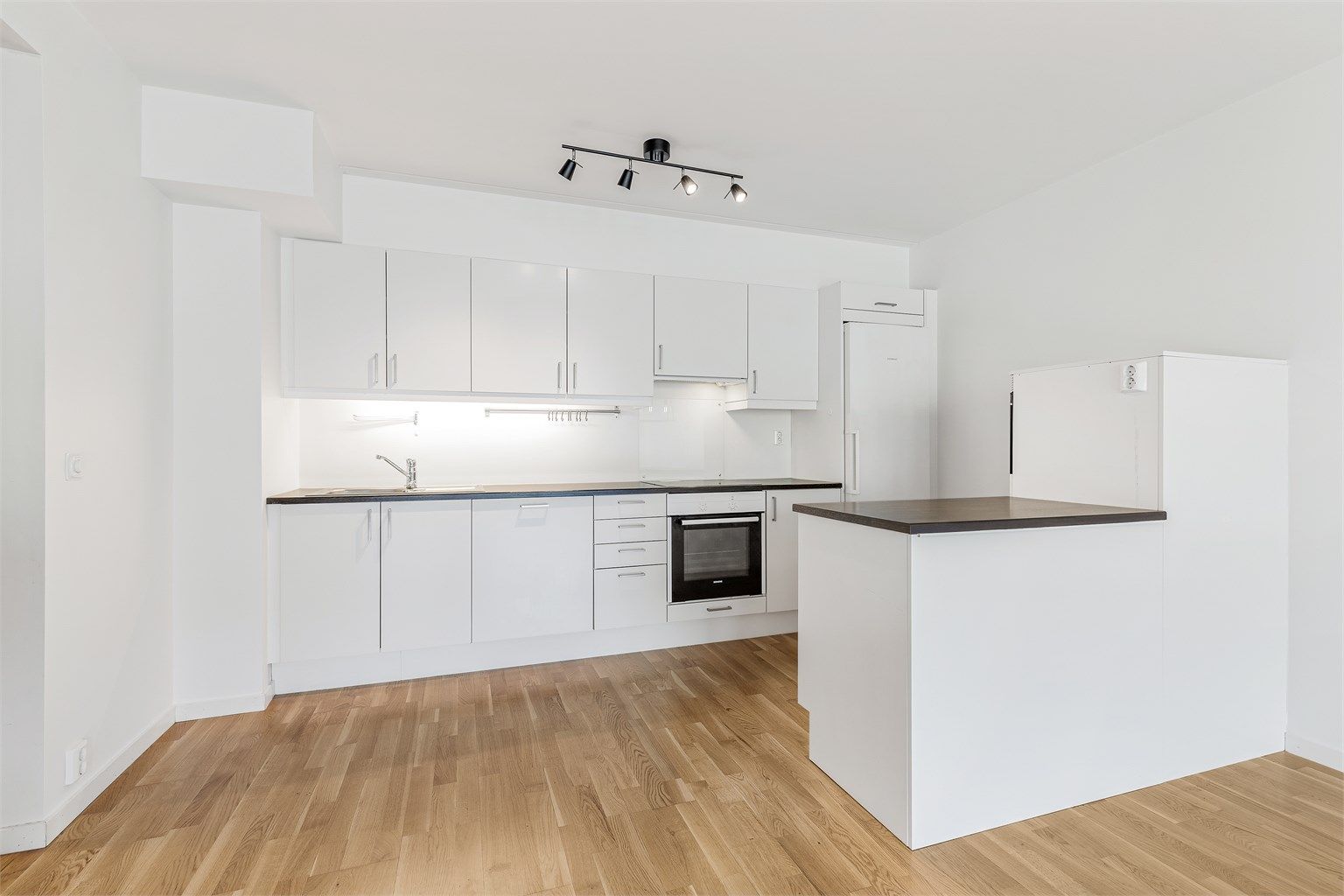 Kjøkken med innredning fra byggeåret. Innredningen har glatte fronter og benkeplater av laminat. Belysning under overskapene.
Foto: Trond Reder