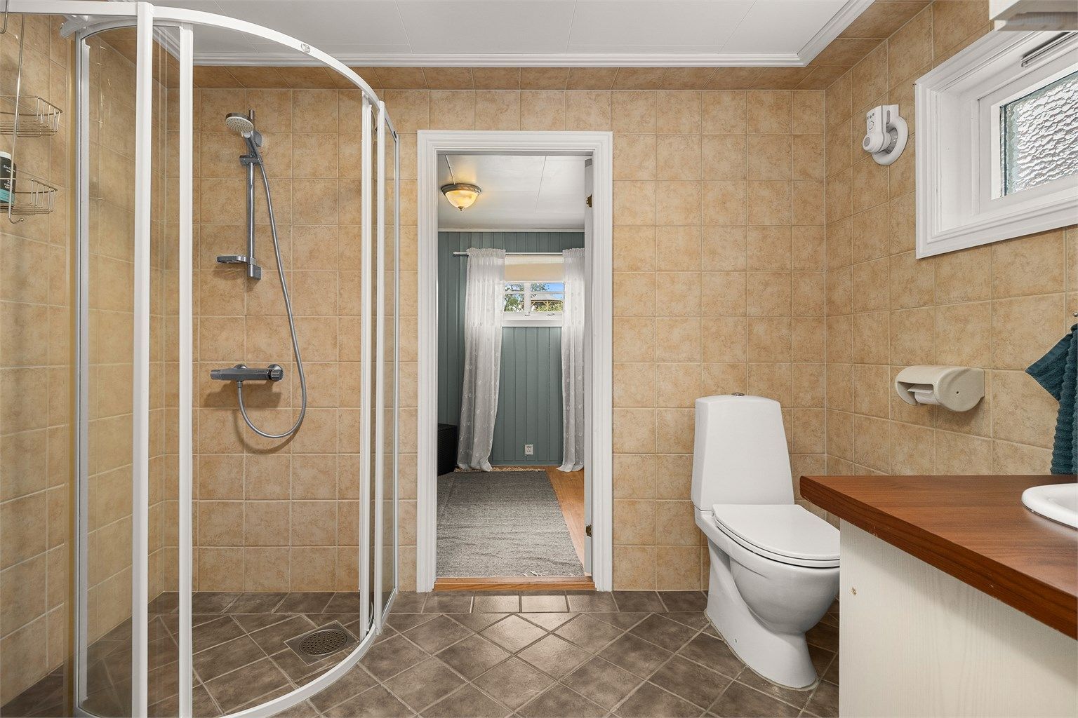 Badet i 1. etasje har dusjløsning, toalett og servantinnredning, og fremstår funksjonelt med lyse overflater.