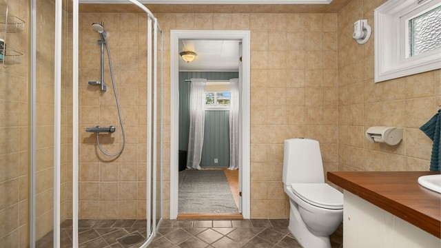 Badet i 1. etasje har dusjløsning, toalett og servantinnredning, og fremstår funksjonelt med lyse overflater.