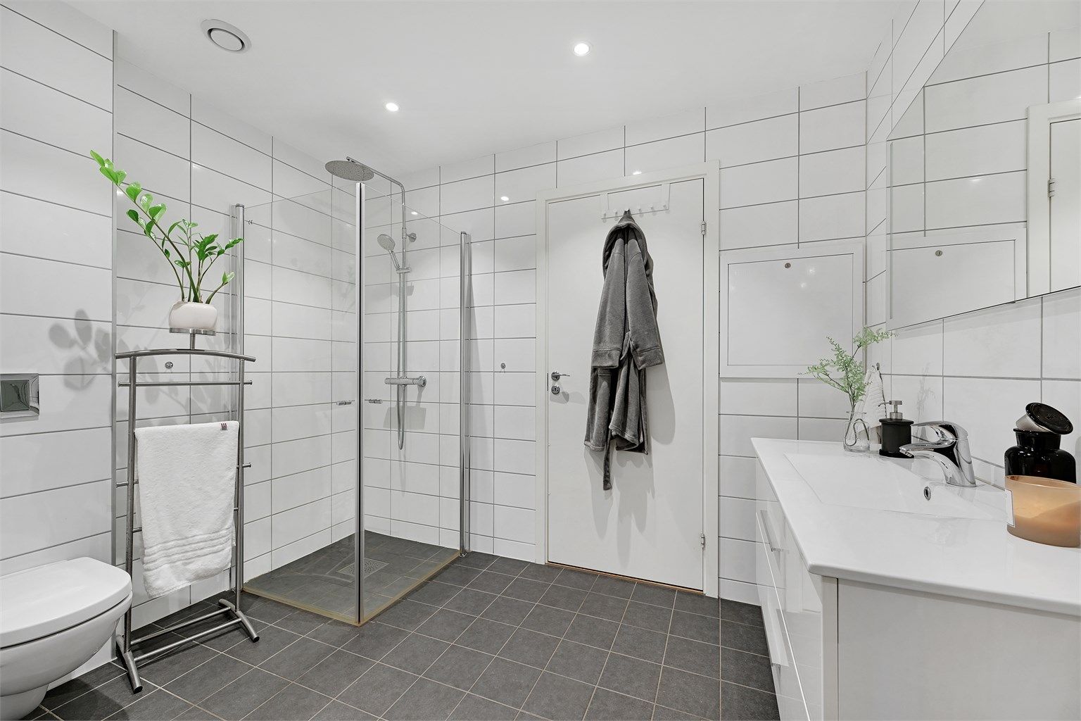 Badet er utstyrt med dusjvegger i glass, veggmontert toalett og servantinnredning.