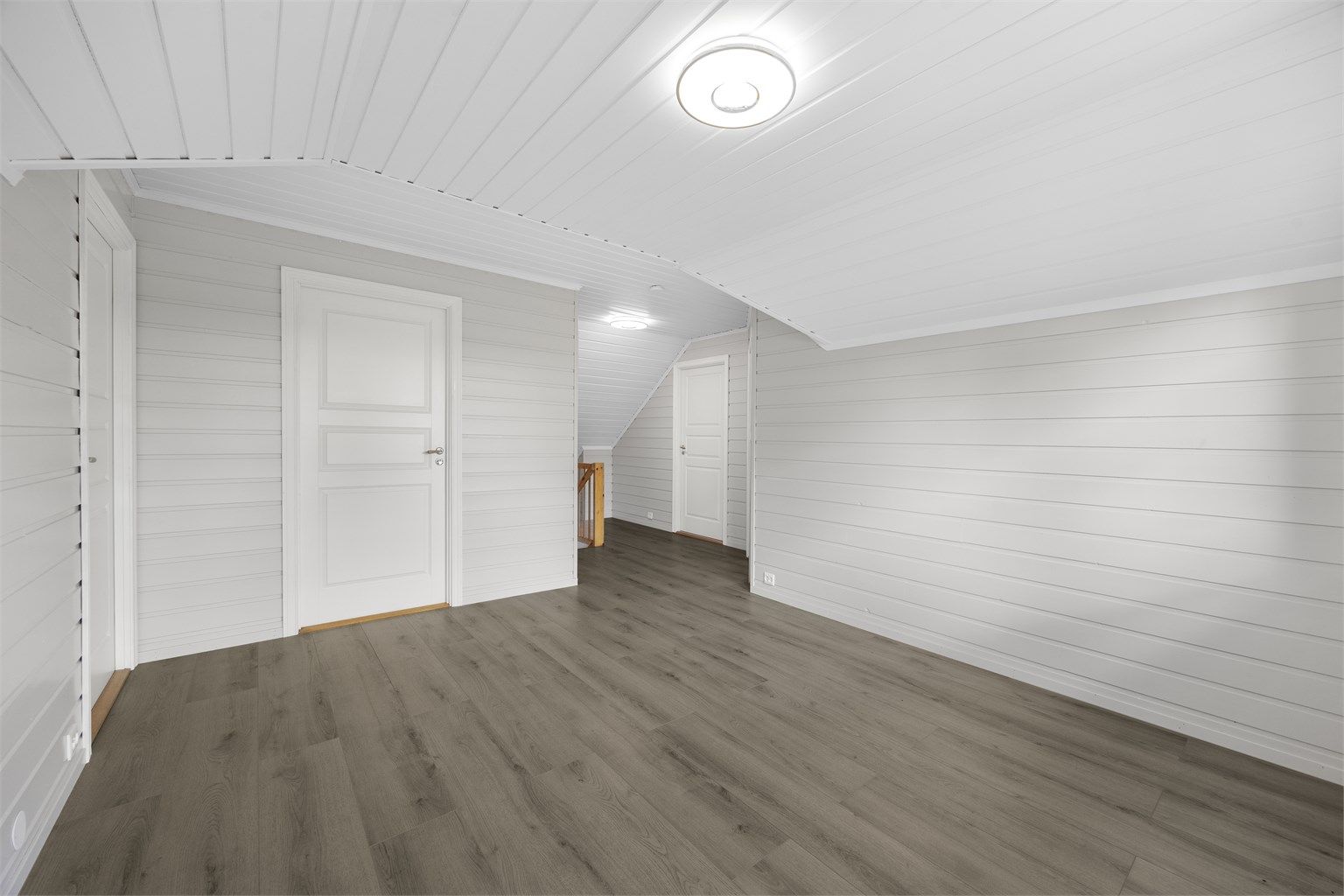 Loftsetasjen har en lys loftstue med hvitmalte panelvegger og laminatgulv.