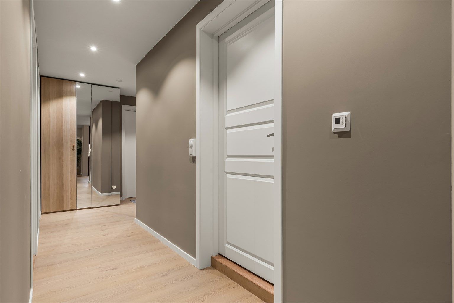 Romslig entré med en-stavs laminatgulv og downlights i himling.