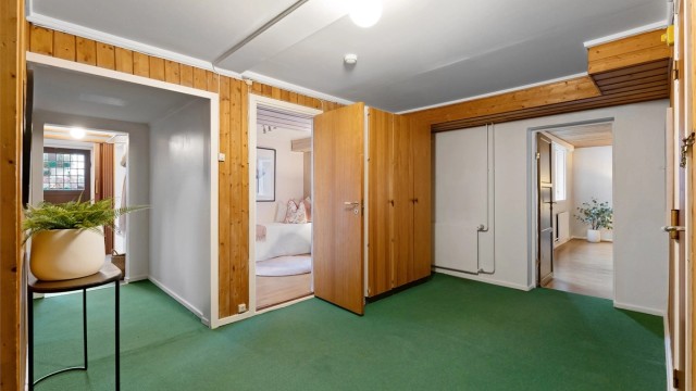 Gang i underetasjen med adkomst til flere innredede rom og trapp opp til første etasje.