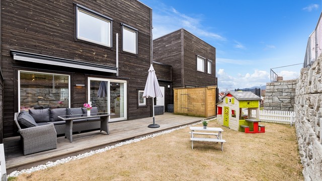 Fra stuesiden er det utgang til en hyggelig markterrasse med fin terrassemarkise og praktisk lagringsbod for utemøbler mm. Fint plenareale som innbyr til lek for viltre småtasser