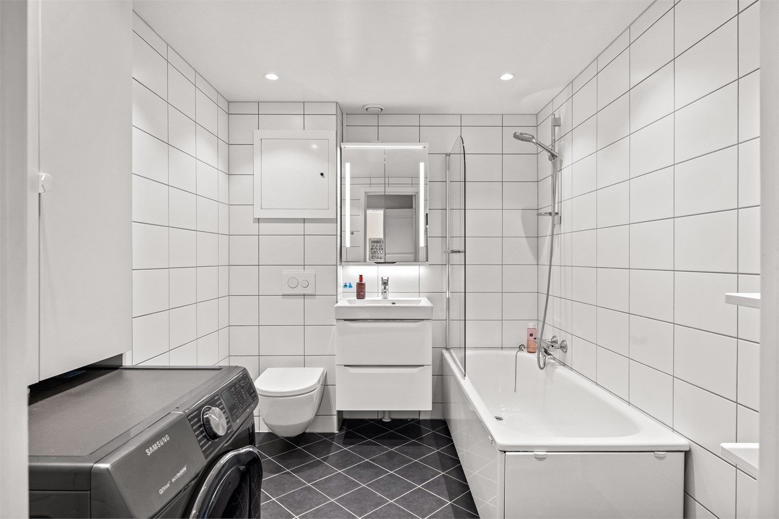 Leilighetens baderom er fra 2019, med flislagt gulv og vegger, samt opplegg for vaskemaskin. Badekar med vegghengt
badekararmatur